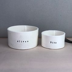 two white bowls sitting on top of a table next to each other with words written in them