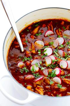 a pot filled with stew and radishes on top of a white tablecloth