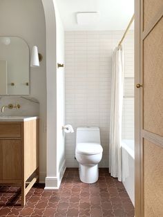 a white toilet sitting next to a bath tub in a bathroom under a light fixture