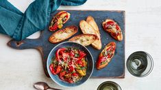 an overhead view of bread, tomatoes and other food items on a cutting board with blue napkins