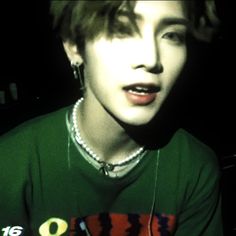 a young man in a green shirt with ear buds on his ears and necklaces around his neck