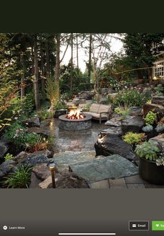 an outdoor fire pit surrounded by plants and rocks in the middle of a garden area