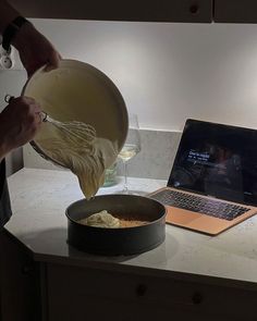 a person pouring something into a bowl on top of a counter next to a laptop