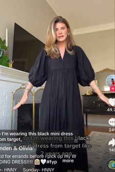 a woman standing in front of a fireplace with her hands on her hips, wearing a black dress