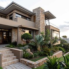 a modern house with landscaping and stone steps leading up to the front door, on a hillside