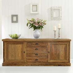 a vase filled with flowers sitting on top of a wooden dresser next to two candles