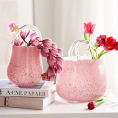 two vases filled with pink flowers sitting on top of a table next to a book