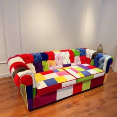 a multicolored couch sitting on top of a hard wood floor next to a white wall