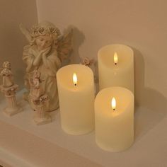 three lit candles sitting on top of a shelf next to an angel figurine