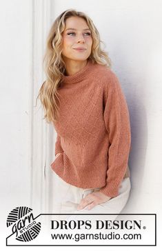 a woman leaning against a wall wearing a brown sweater