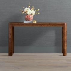 a vase with flowers sitting on top of a wooden table next to a gray wall