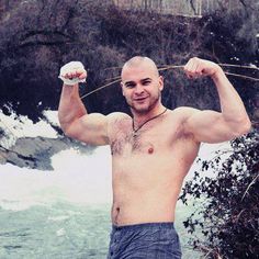 a shirtless man standing in front of a river holding two frisbees