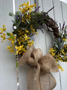 a wreath with yellow and purple flowers hanging on the side of a white wooden fence