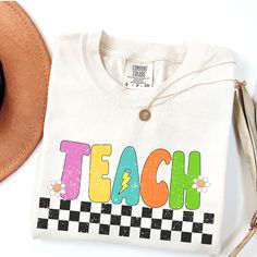 These soft  Comfort Colors shirts are printed with a retro checkered TEACH graphic with cute smiley face flowers and lightning bolt pencil. Perfect for the cool teacher going back to school to TEACH :)  * 100% ring-spun cotton * Fabric weight: 6.1 oz/yd² (206.8 g/m²) * Garment-dyed * Relaxed fit * 7/8″ double-needle topstitched collar * Twill-taped neck and shoulders for extra durability * Double-needle armhole, sleeve, and bottom hems SIZING:  They're unisex but fit true to size (or very close to) for ladies. We recommend sizing up though if you prefer a roomier or oversized look! Guys, we definitely suggest sizing up. As these shirts are personalized we do not offer exchanges or refunds unless an error has been made so please check measurement chart before ordering. We would love to assi Cheap Retro Letter Print T-shirt, Cheap Retro T-shirt With Letter Print, Cheap Playful School Shirt, Teach Shirt, Smiley Flower, Cute Smiley Face, Flower Face, Teaching Shirts, Comfort Colors Tshirt