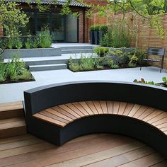 a curved bench sitting on top of a wooden floor next to a lush green garden