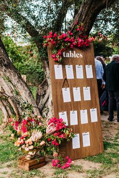 a wooden table with seating cards and flowers on it next to a tree in the grass