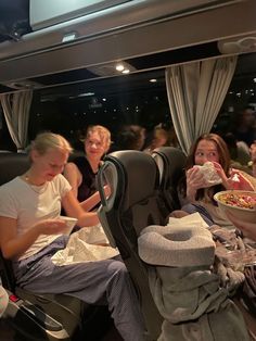 three women sitting on a bus eating food