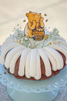 a winnie the pooh bundt cake with frosting and flowers on top is sitting on a blue plate