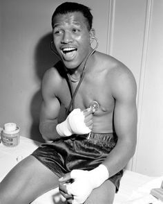 a shirtless man sitting on a bed with bandages around his ankles and holding a tube