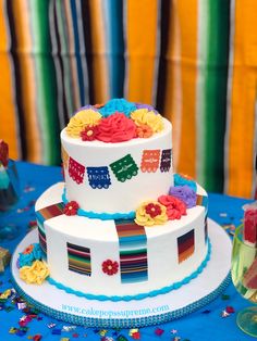 a three tiered cake decorated with colorful flowers and train decorations on a blue table cloth