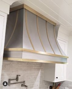 an oven hood in the middle of a kitchen with white cabinets and marble counter tops