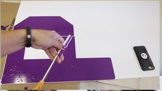 a person using a pair of scissors to cut out the letter e on a piece of purple paper