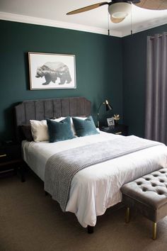 a bedroom with green walls, white bedding and a gray foot stool in front of the bed