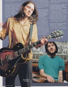 a man holding a guitar while standing next to another man