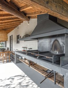 an outdoor kitchen with a large stove and dining table in the back ground, surrounded by wood beams