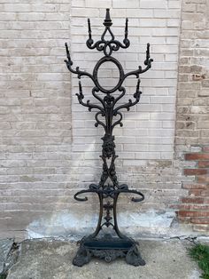 a wrought iron candelabra stands in front of a brick wall