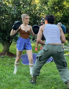 two people in the grass playing frisbee with one person wearing shorts and a tank top