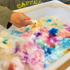 a child's hand is writing on the paper that has been dyed with colored dye