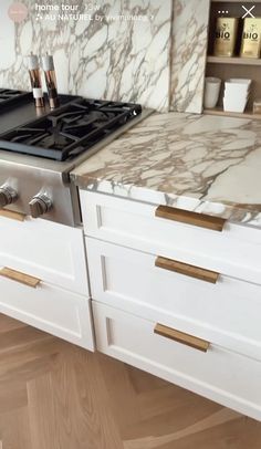 a stove top oven sitting inside of a kitchen next to white cupboards and drawers