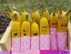 a bunch of bananas with faces drawn on them sitting in a wooden box next to purple ribbon