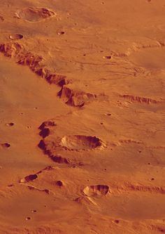 footprints in the sand on an orange colored beach area with small rocks and water at the bottom