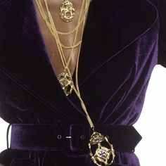 a close up of a person wearing a purple jacket and gold necklace with chains on it