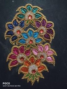 an embroidered brooch with multicolored flowers and leaves on the side, sitting on a black surface