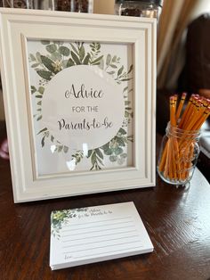 a wooden table topped with a framed sign next to a vase filled with pencils