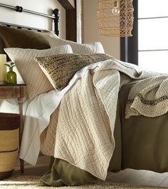 a bed covered in blankets and pillows next to a table with vases on it