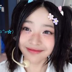 a woman with black hair wearing a white shirt and pink flowers in her hair is smiling at the camera