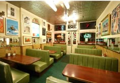 the inside of a restaurant with green booths and wooden tables, framed pictures on the wall