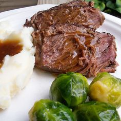 a white plate topped with meat and mashed potatoes next to brussel sprouts