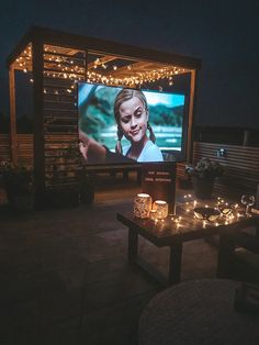 an outdoor movie screen is lit up at night with candles on the table and lights around it