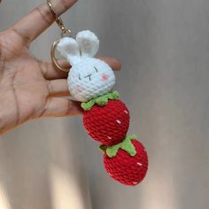 a hand holding a small stuffed animal with two strawberries attached to it