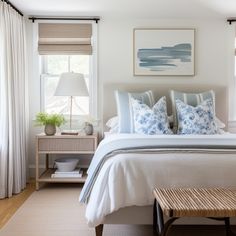 a white bed with blue and white pillows on top of it next to a window