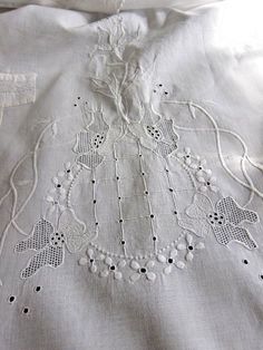 an embroidered piece of cloth with white thread and beads on the edges, sitting on top of a bed