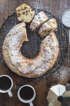 a cake sitting on top of a cooling rack next to two cups of coffee