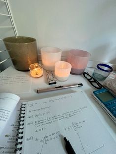 a notebook with some writing on it next to two candles and a calculator