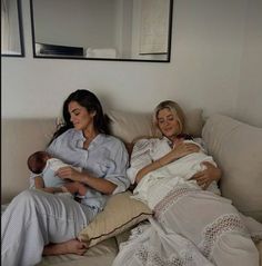 two women sitting on a couch holding babies