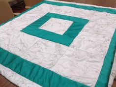 a large green and white quilt sitting on top of a wooden floor next to a box